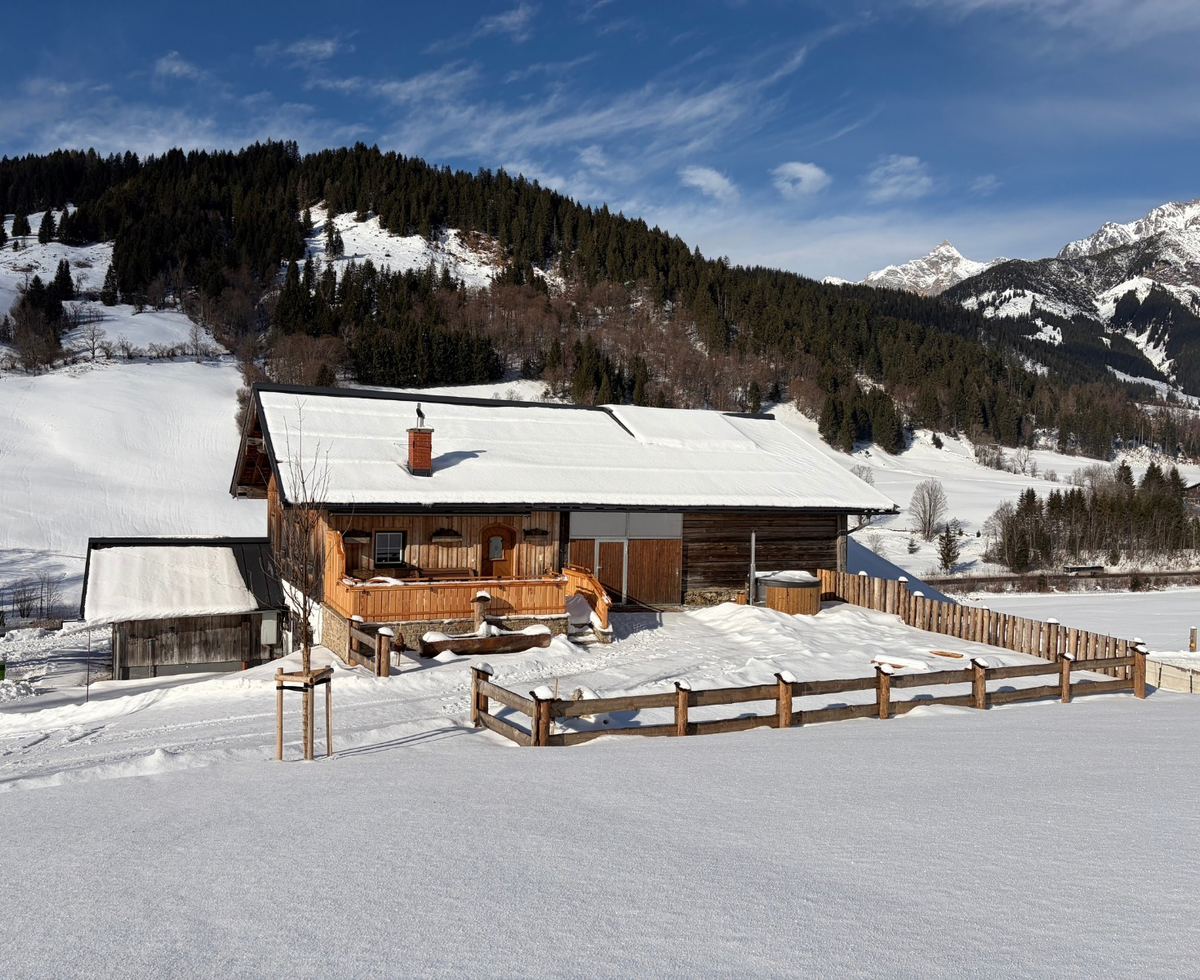 Die Alm in einer verschneiten Winterlandschaft mit Bergen und einem Außen-Whirlpool.