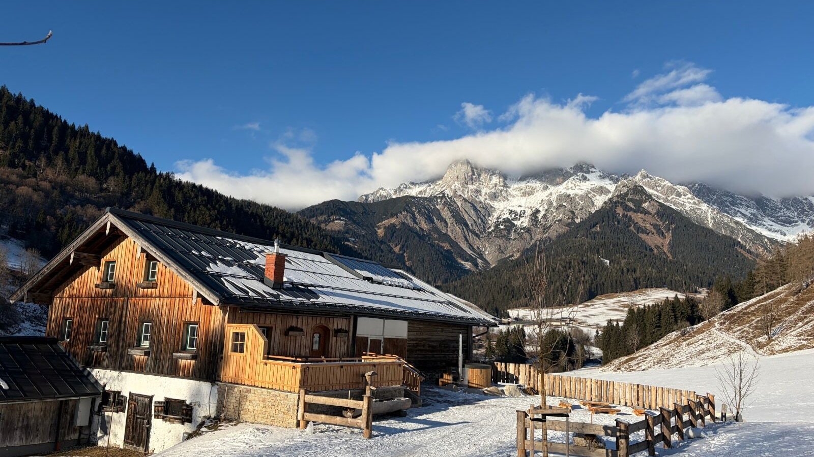 Die Alm in einer verschneiten Berglandschaft mit Holzbalkon und Blick auf die schneebedeckten Berge.