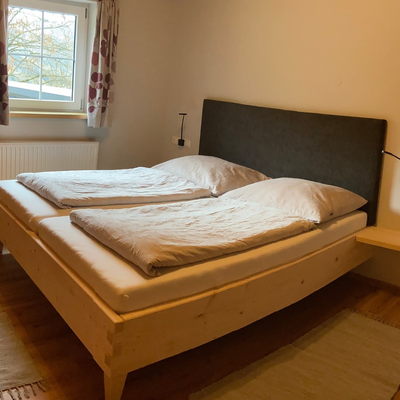 Schlafzimmer der Alm mit Doppelbett, Holzbettrahmen, Leselampen und Fenster.