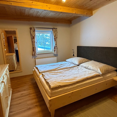 Schlafzimmer der Alm mit Doppelbett, Holzmöbeln, Fenster und Holzbalkendecke.