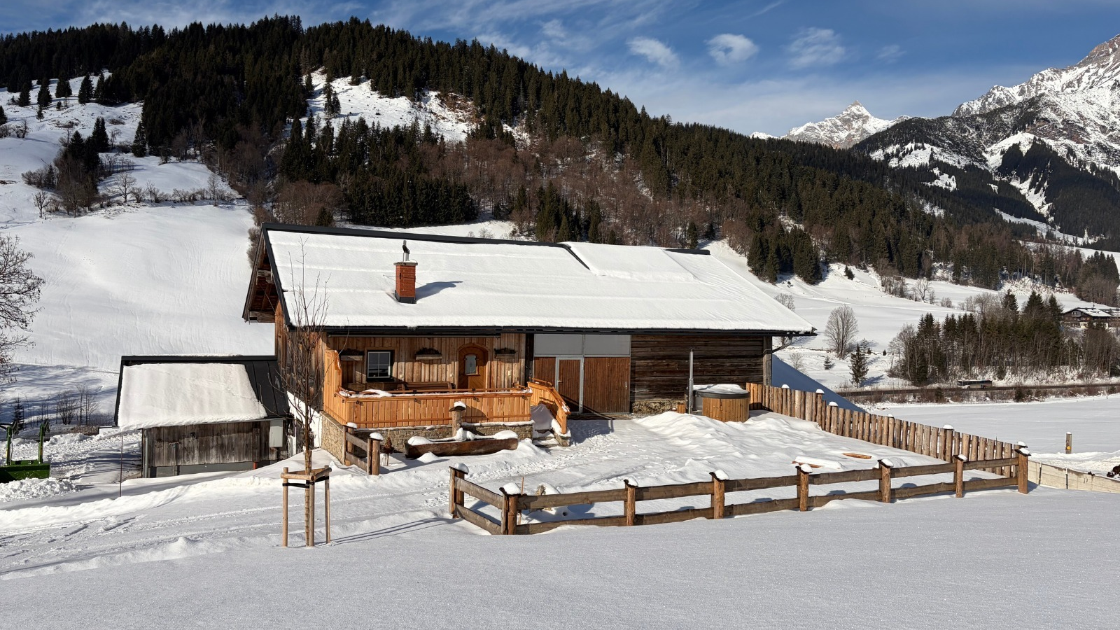 Die Alm in einer verschneiten Winterlandschaft mit Bergen und einem Außen-Whirlpool.