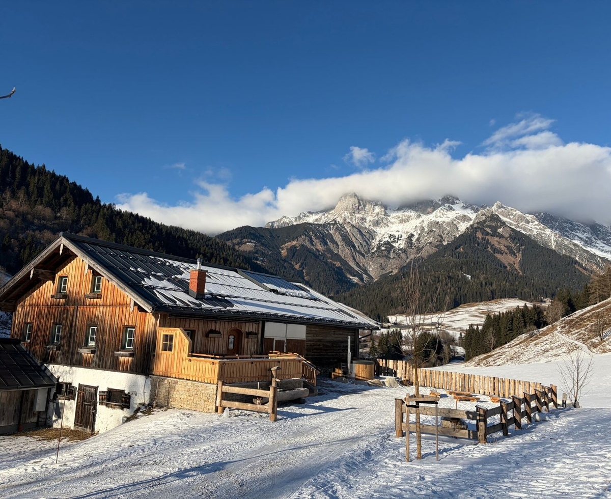 Die Alm in einer verschneiten Berglandschaft mit Holzbalkon und Blick auf die schneebedeckten Berge.