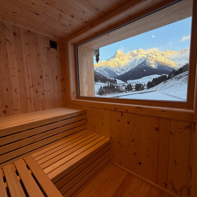 Die Sauna der Alm mit Holzbänken und einem großen Fenster, das einen Panoramablick auf die verschneiten Berge und das Tal bietet.