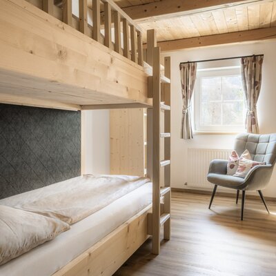 Schlafzimmer der Alm mit Holzetagenbett, Fenster und Sessel.