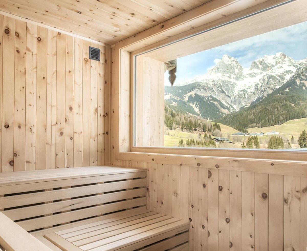 Sauna der Alm mit Holzbänken und großem Fenster mit Bergblick.