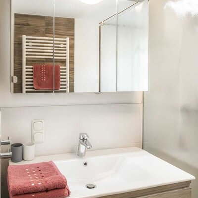 Badezimmer in der Alm mit Waschbecken, Holzunterschrank, beleuchtetem Spiegelschrank und Handtuchheizkörper.