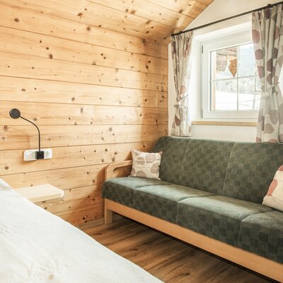 Schlafzimmer in der Alm mit Holzwänden, einem Bett, einem Fenster und einem grünen Sofa.