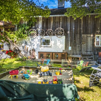 Der Gartenbereich des Bauernhofs mit Sandkasten, Spielzeug und Sonnenliegen.