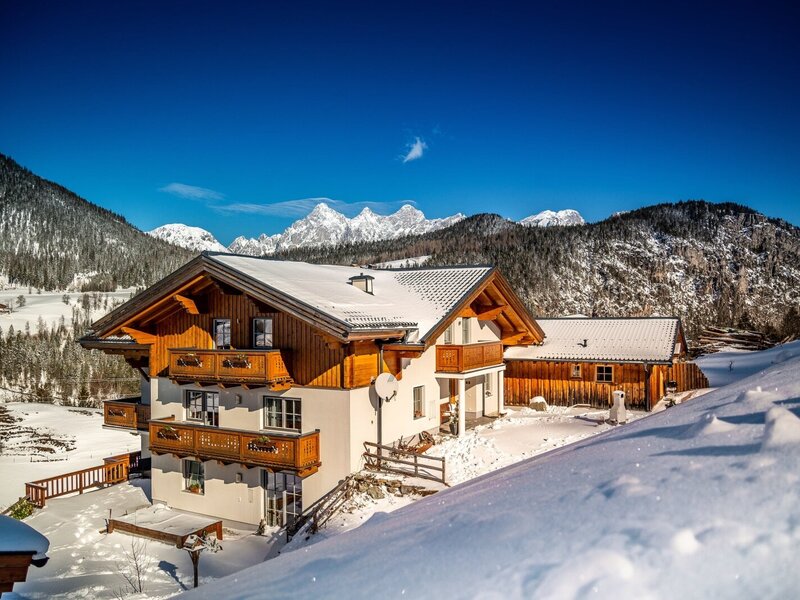 Außenansicht des Bauernhofs im Winter, mit verschneiter Landschaft, Bergblick und hölzernen Balkonen.