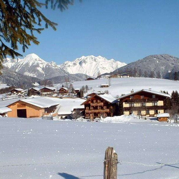 Der Bauernhof in einer verschneiten Winterlandschaft mit Blick auf die umliegenden Berge.
