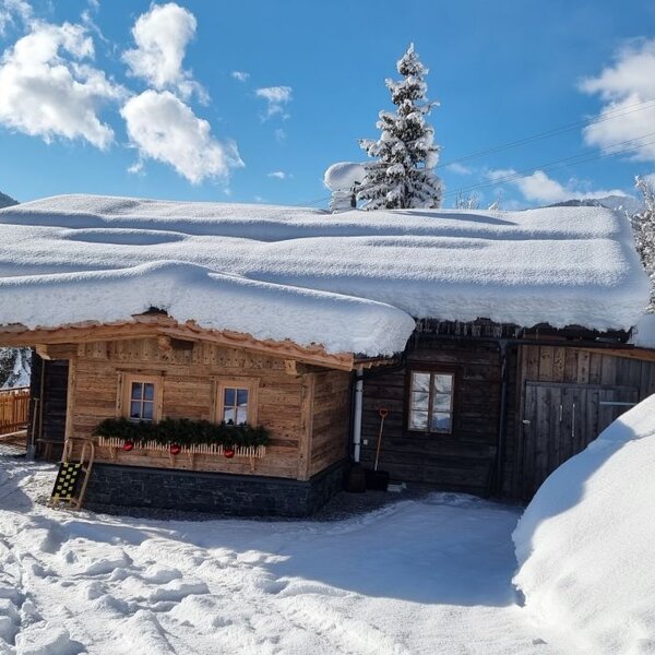 Der schneebedeckte Hof mit Holzfassade und dekorierten Fenstern vor winterlicher Bergkulisse.
