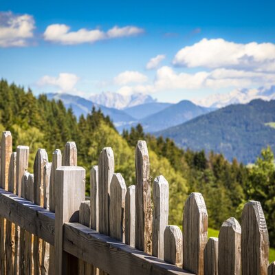 Holzzaun mit Blick auf die umliegende Berglandschaft vom Hof.