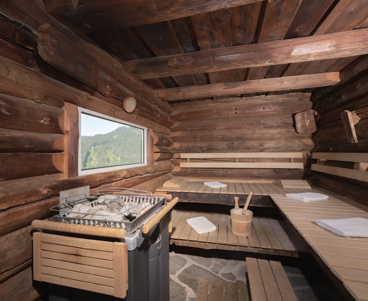 Die Sauna im Bauernhof mit Holzbalken, Saunaofen und Fenster mit Bergblick.