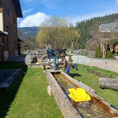 Kinderspielbereich auf dem Bauernhof mit Wasserrinne und Handpumpe.
