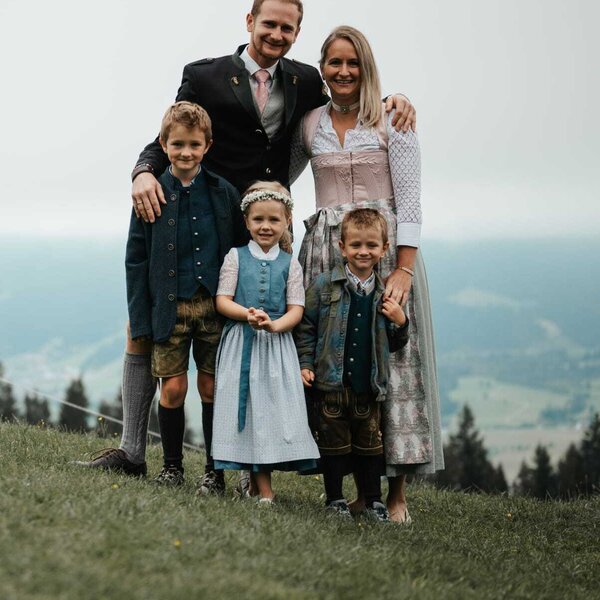 Die Gastgeberfamilie des Bauernhofs in traditioneller Kleidung vor einer Berglandschaft.
