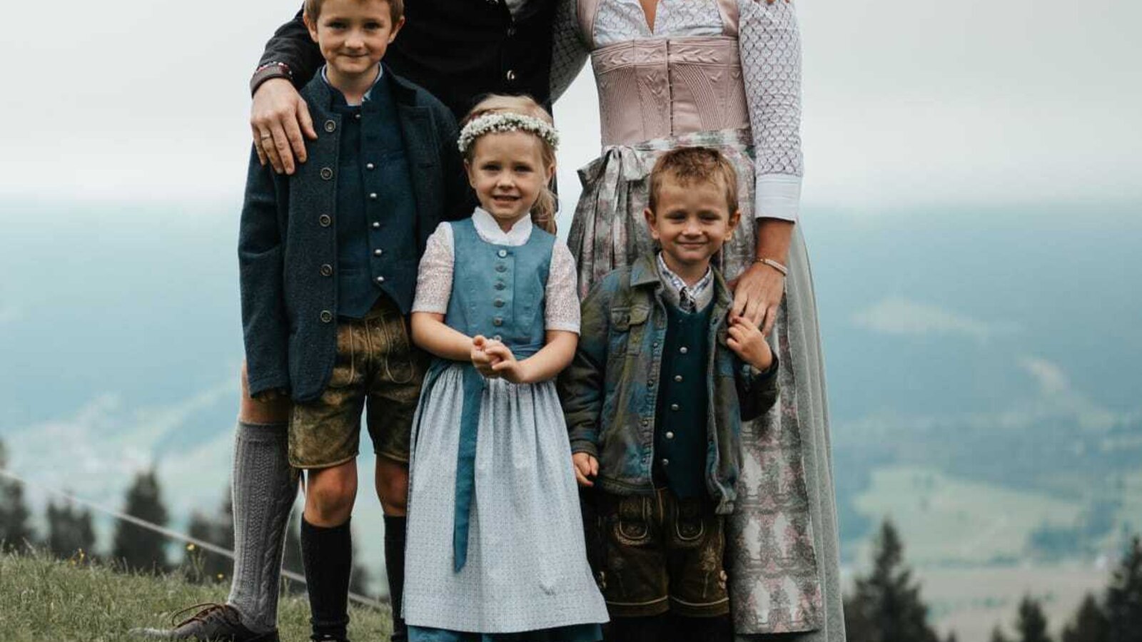 Die Gastgeberfamilie des Bauernhofs in traditioneller Kleidung vor einer Berglandschaft.