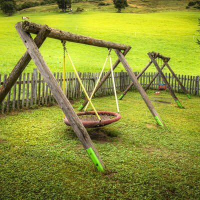 Ein einladender Spielplatz am Bauernhof mit Holzschaukeln und Blick auf die saftig grünen Wiesen.