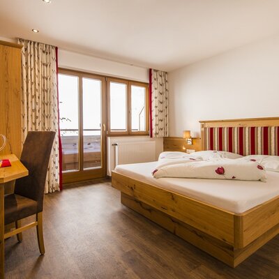 Doppelzimmer im Ferienbauernhof mit Holzdoppelbett, Schreibtisch, Fernseher und Balkonzugang.