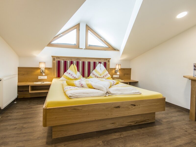 Doppelzimmer im Ferienbauernhof mit Holzbett, gepolstertem Kopfteil, Nachttischen und dreieckigen Dachfenstern.