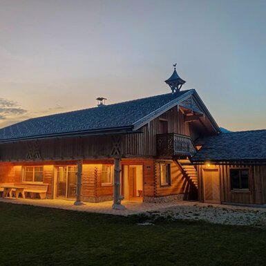 Der Bauernhof am Abend, mit beleuchteter Holzveranda und Sitzgelegenheiten.