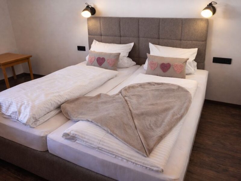 Schlafzimmer mit einem Doppelbett, gepolstertem Kopfteil, Wandleuchten und einem kleinen Beistelltisch.