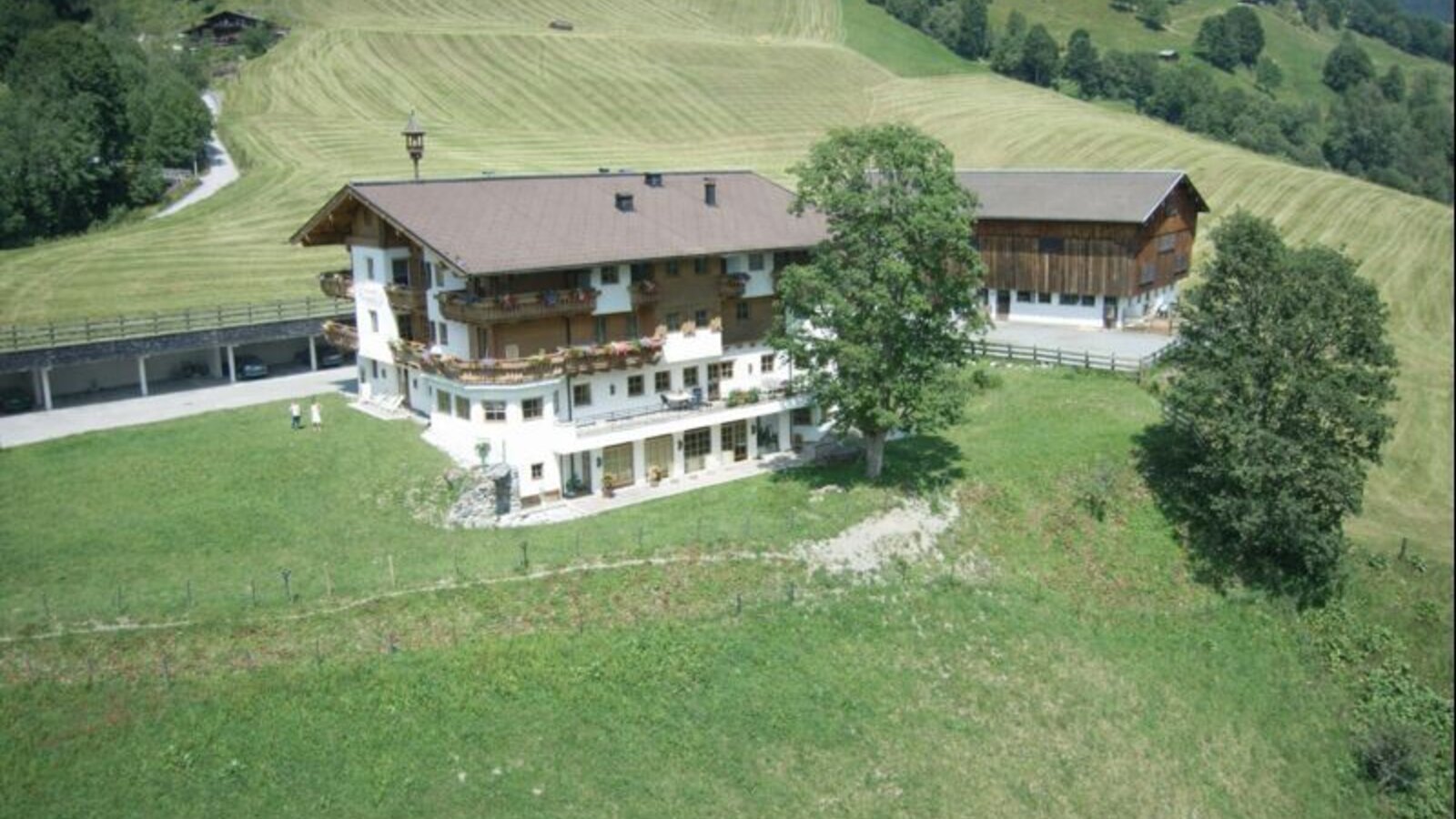 Außenansicht mit umliegenden Feld, einem Nebengebäude und überdachten Parkplätzen.