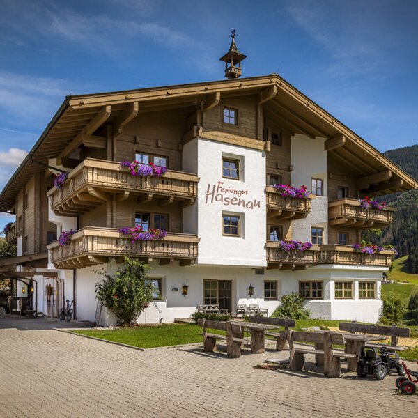 Die charmante Außenansicht des Bauernhofs im alpinen Stil mit blumengeschmückten Holzbalkonen und einem einladenden Sitzbereich im Freien.