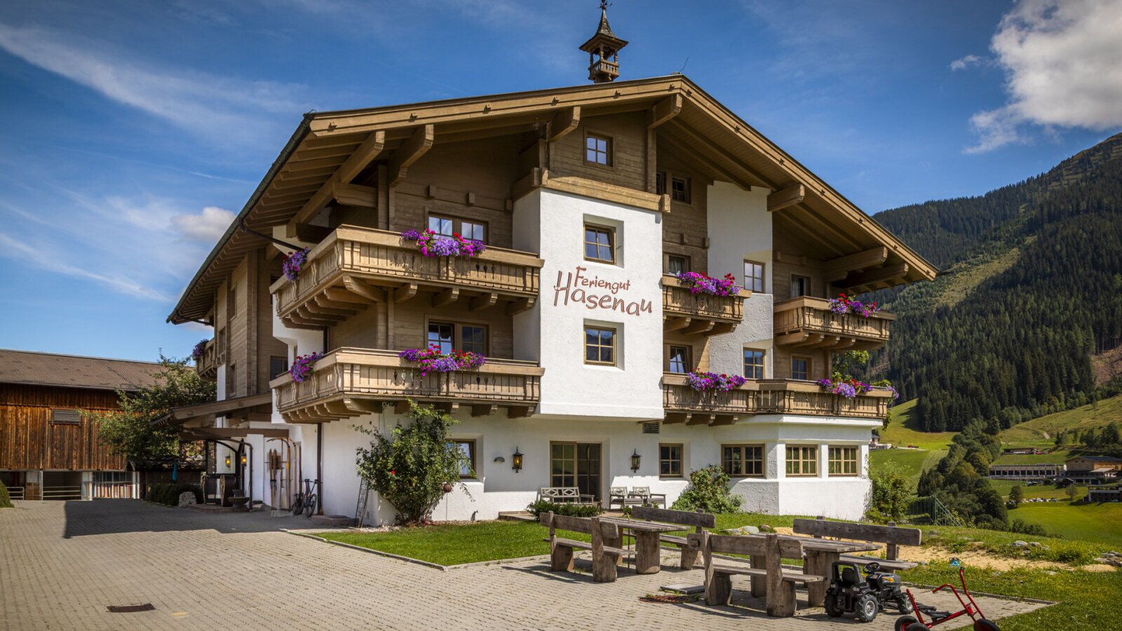 Die charmante Außenansicht des Bauernhofs im alpinen Stil mit blumengeschmückten Holzbalkonen und einem einladenden Sitzbereich im Freien.