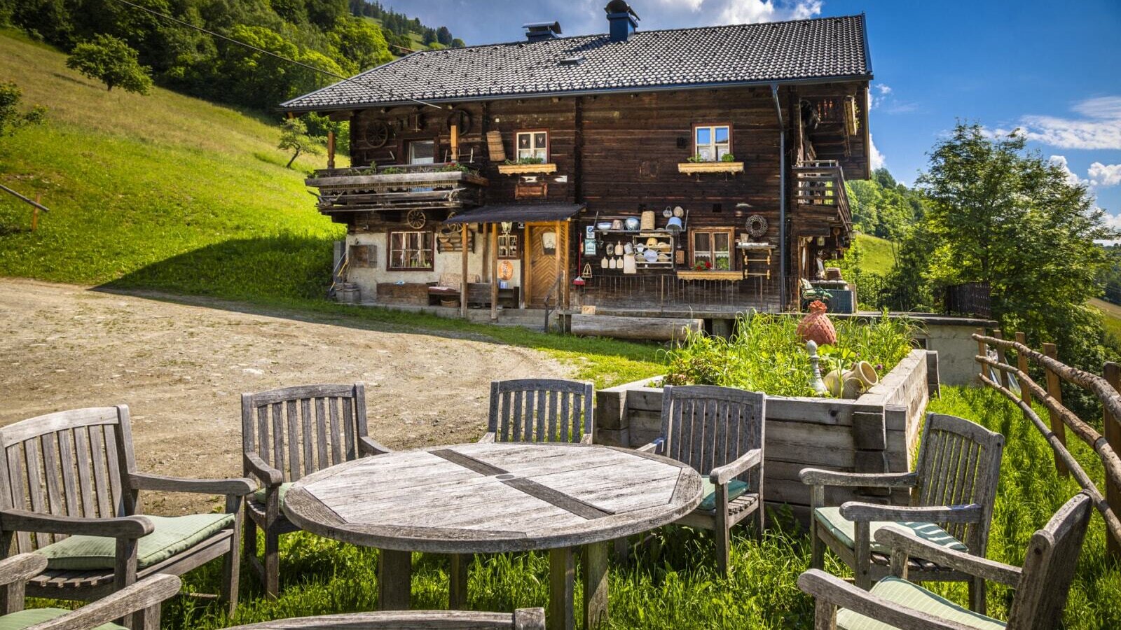 Außensitzbereich mit Holztisch und Stühlen mit grünen Polstern auf der Wiese vor dem Ferienhaus.