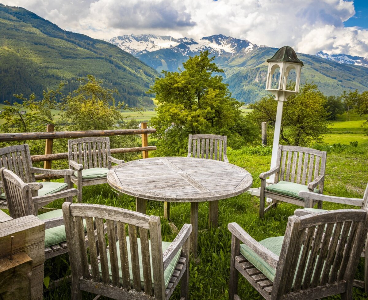 Der Außenbereich des Ferienhauses bietet eine Holz-Sitzgruppe mit Blick auf grüne Täler und schneebedeckte Berge.
