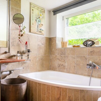 Badezimmer des Ferienhauses mit Badewanne, Waschbecken mit roter Ablage und einem Fenster.