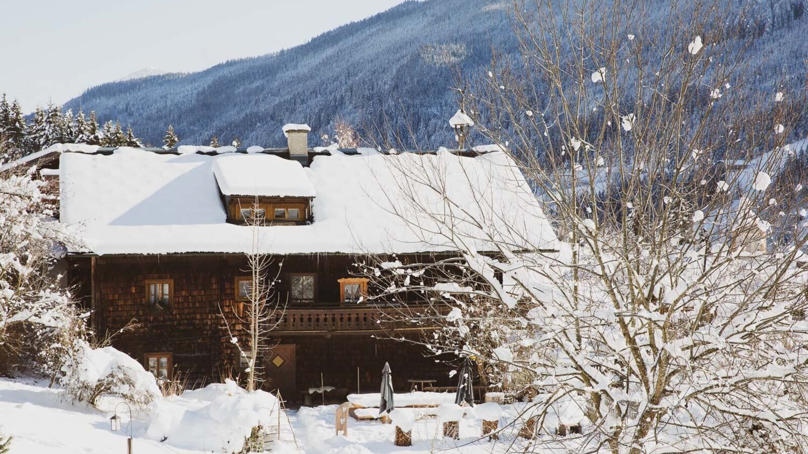Das Ferienhaus im Winter, mit schneebedecktem Dach, Holzbalkon und einem Außensitzbereich. Copyright: Urlaub am Bauernhof / Pascal Baronit