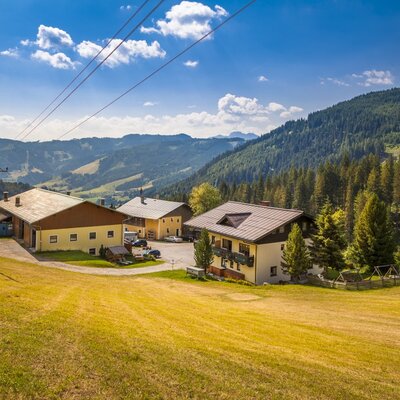 Der Hof eingebettet in die grüne Berglandschaft, umgeben von Wiesen und Wäldern.