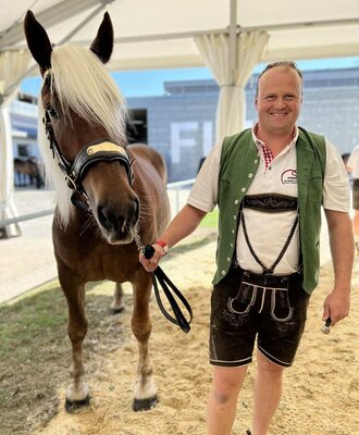 Ein freundlicher Gastgeber in traditioneller Tracht präsentiert ein prachtvolles Pferd des Bauernhauses.
