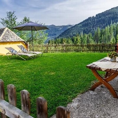 Der einladende Garten des Bauernhauses mit einer gepflegten Liegewiese, Sonnenstühlen und einer gemütlichen hölzernen Sitzecke mit Blick auf die Berge.