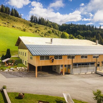 Das traditionelle Gebäude des Bauernhofs, umgeben von saftig grünen Wiesen und bewaldeten Hügeln.