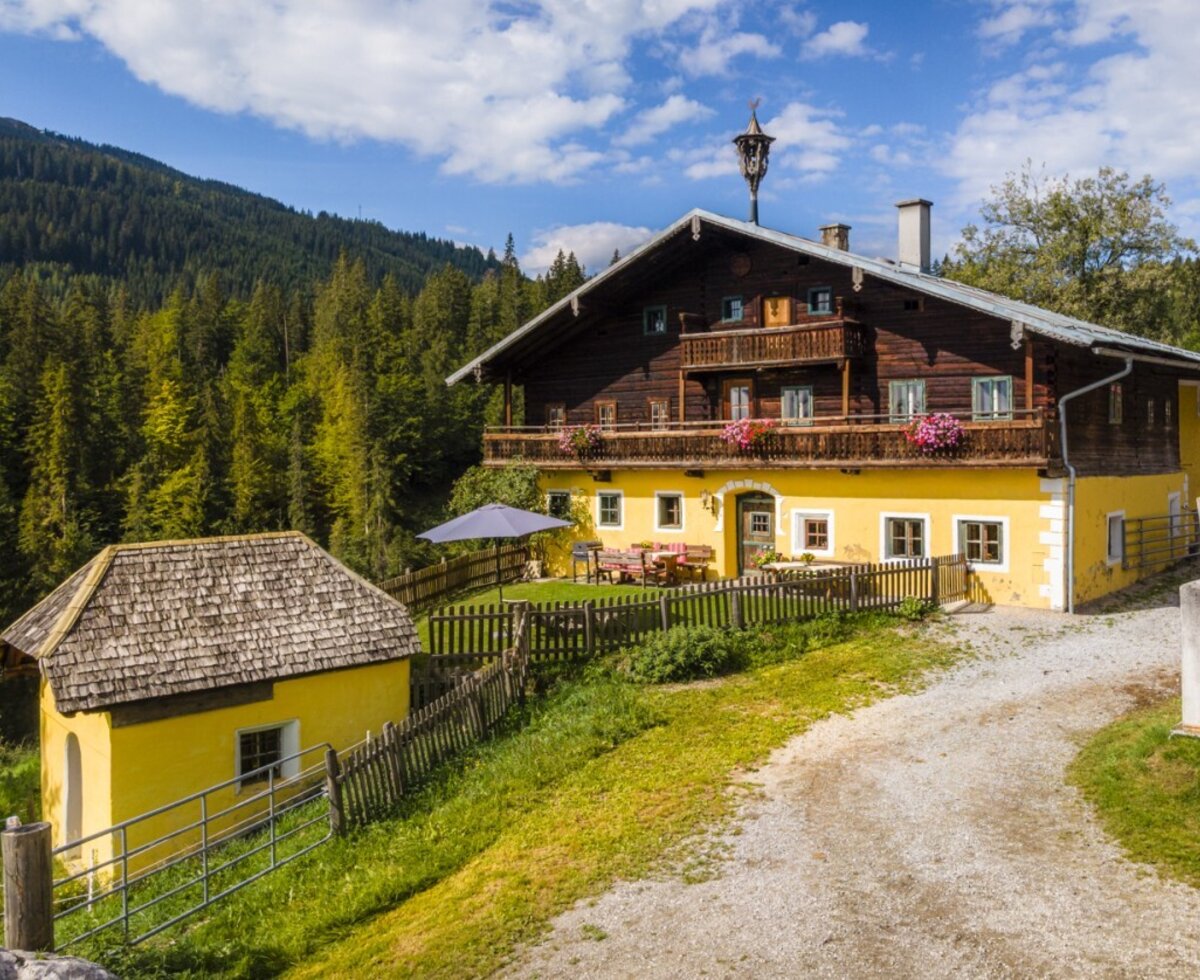 Das historische Bauernhaus mit seinen charmanten Holzbalkonen, eingebettet in eine idyllische Wald- und Berglandschaft.
