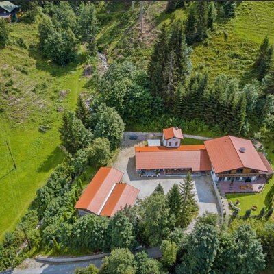 Luftaufnahme der Ferienwohnung mit mehreren Gebäuden, umgeben von grünen Hügeln und Wald.