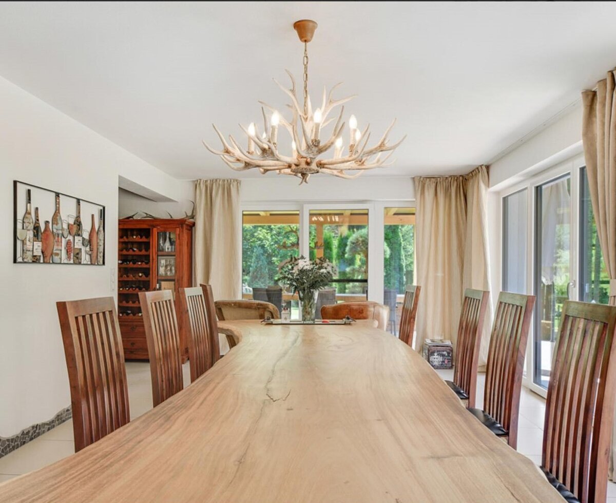 Esszimmer der Ferienwohnung mit großem Holztisch, Stühlen, Geweih-Kronleuchter und Zugang zum Garten.