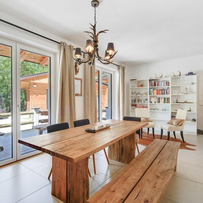 Essbereich der Ferienwohnung mit großem Holztisch, Bank und Stühlen, großen Glastüren zur Terrasse und Bücherregalen.