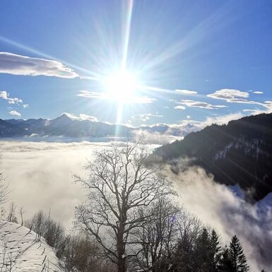Winterlandschaft mit Schnee, Bergen, Nebelmeer und strahlendem Sonnenschein am Hof.
