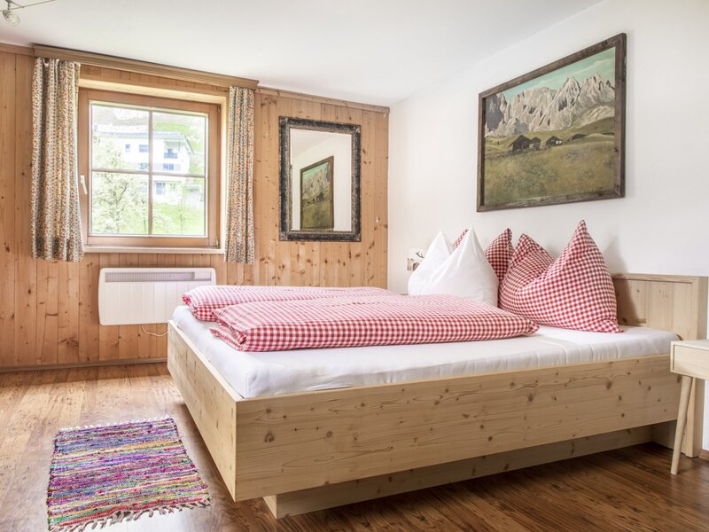 Schlafzimmer im Hof mit Doppelbett, Holzboden und -wänden, Fenster, Heizung und einem Wandbild mit Berglandschaft.