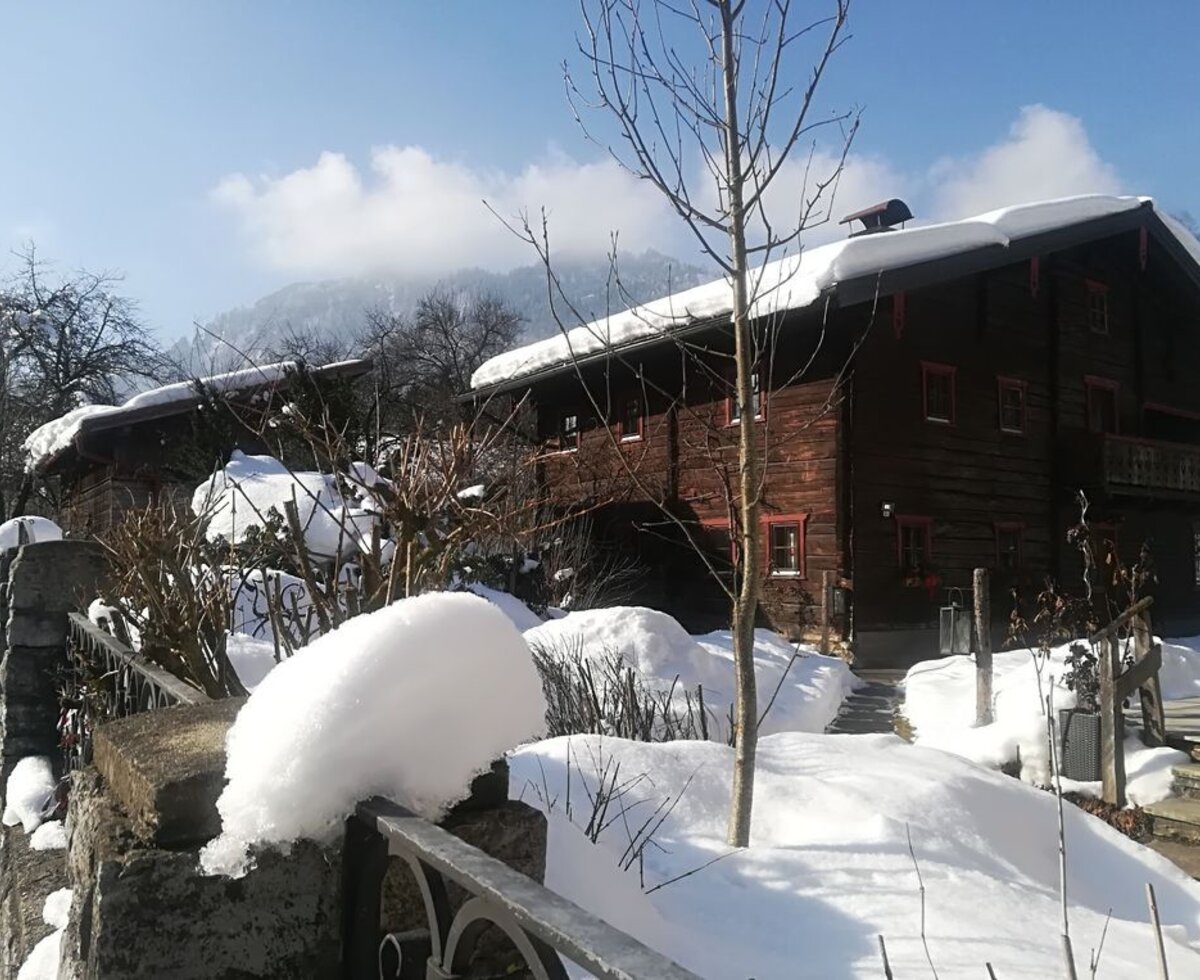 Das traditionelle Hofgebäude aus Holz im Winter, mit schneebedeckten Dächern und Bergblick.