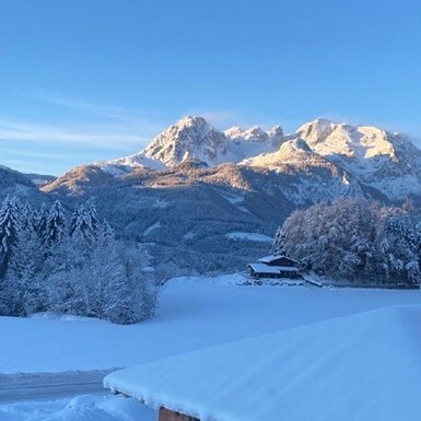 Die winterliche Berglandschaft mit dem Bauernhaus, umgeben von schneebedeckten Feldern und Wäldern.