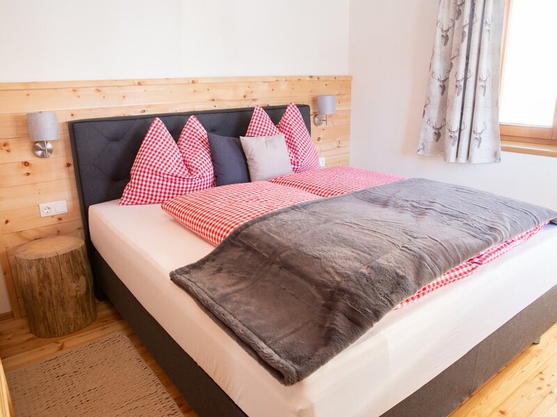 Schlafzimmer im Bauernhof mit Doppelbett, rot-weiß karierter Bettwäsche und einem Baumstamm als Nachttisch.