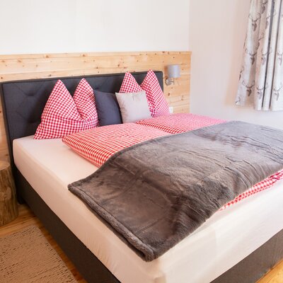 Schlafzimmer im Bauernhof mit Doppelbett, rot-weiß karierter Bettwäsche und einem Baumstamm als Nachttisch.