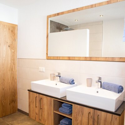Badezimmer im Bauernhof mit Doppelwaschbecken, Holzunterschränken, großem Spiegel, Dusche und Holztür.