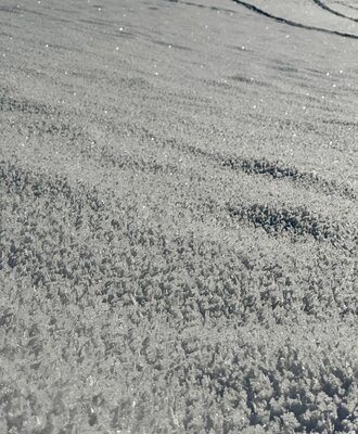 Nahaufnahme von Schnee mit sichtbaren Eiskristallen, die die Winterlandschaft des Ferienhauses prägen.