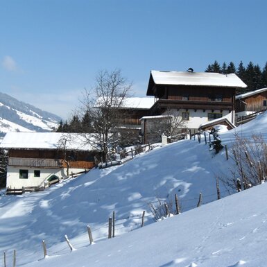 Die traditionellen Gebäude des Hofes im Winter, gelegen auf einem schneebedeckten Hang mit Blick auf die Berge.