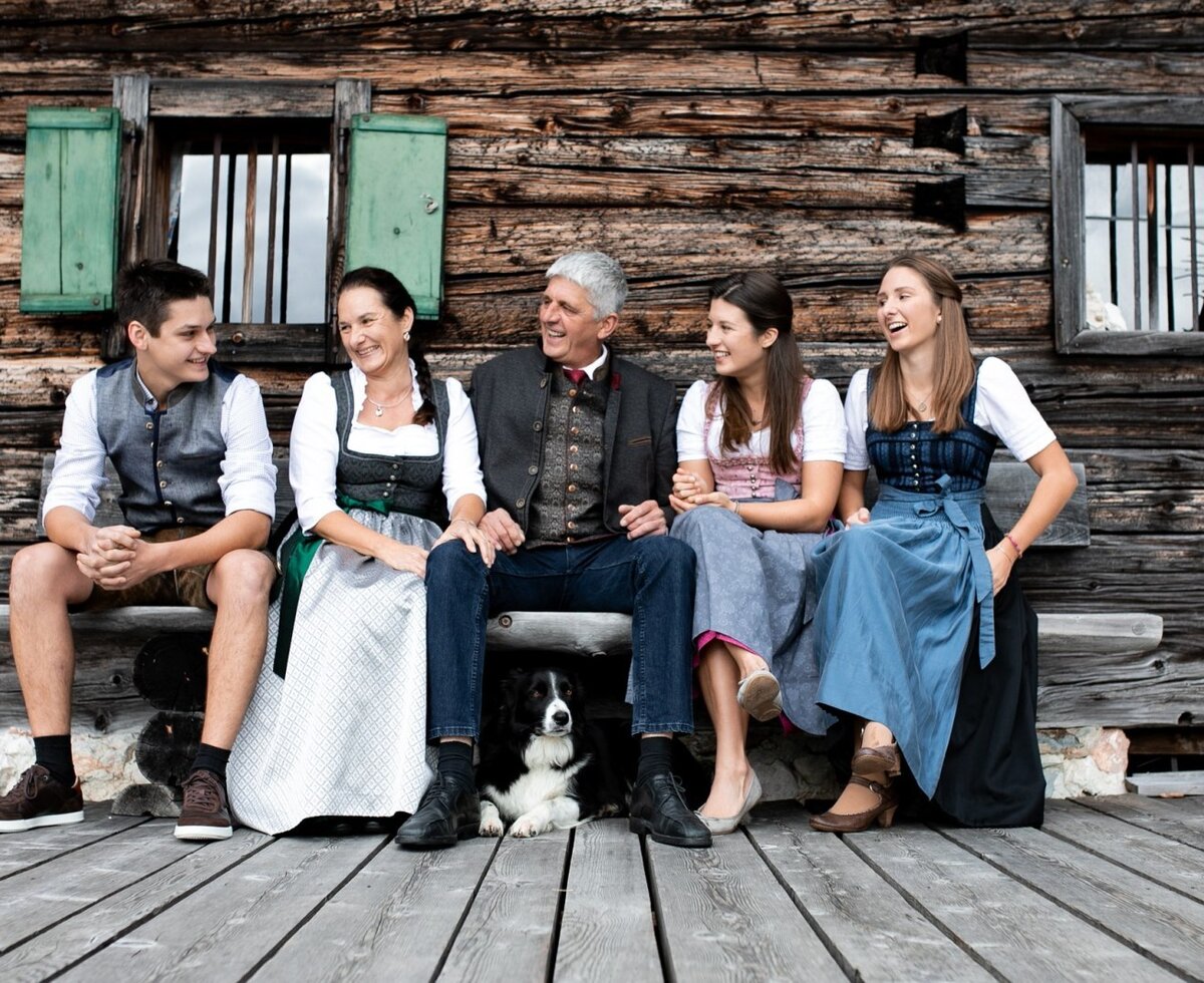 Familie Vitzthum sitzt mit ihrem Hund auf einer Holzbank vor der Almhütte.